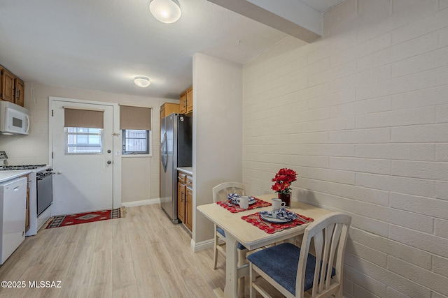 dining area featuring brick wall, light wood-style flooring, and beamed ceiling