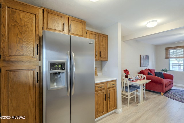 kitchen featuring light countertops, brown cabinets, light wood-type flooring, stainless steel refrigerator with ice dispenser, and open floor plan
