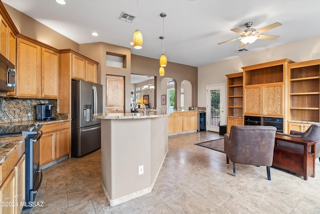 kitchen featuring decorative light fixtures, stainless steel appliances, an island with sink, backsplash, and light stone counters