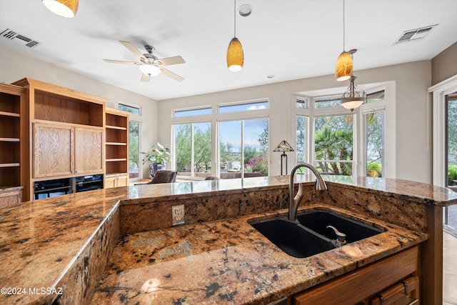 kitchen with ceiling fan, decorative light fixtures, dark stone counters, and sink