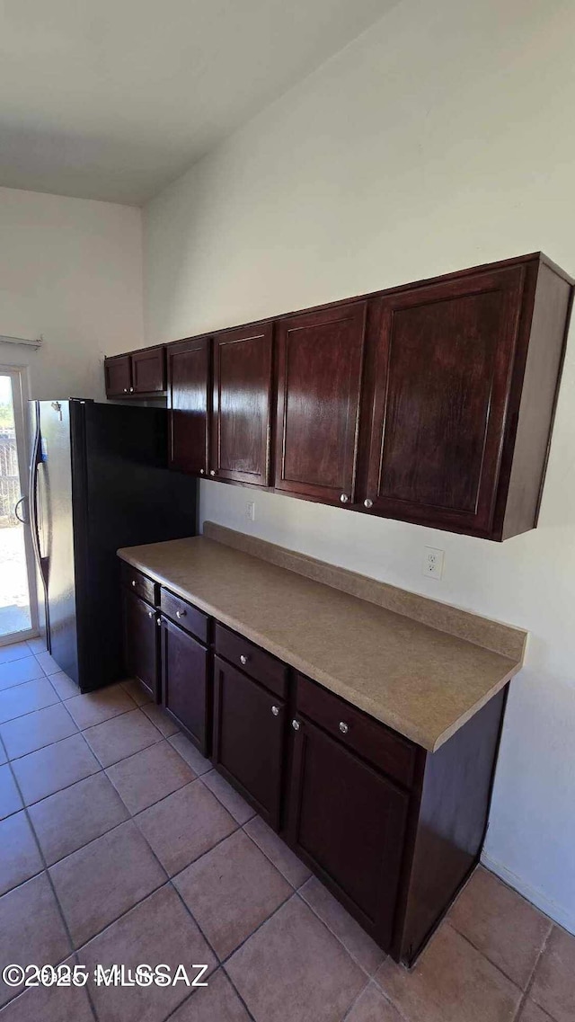 kitchen with black fridge, dark brown cabinetry, and light tile patterned floors