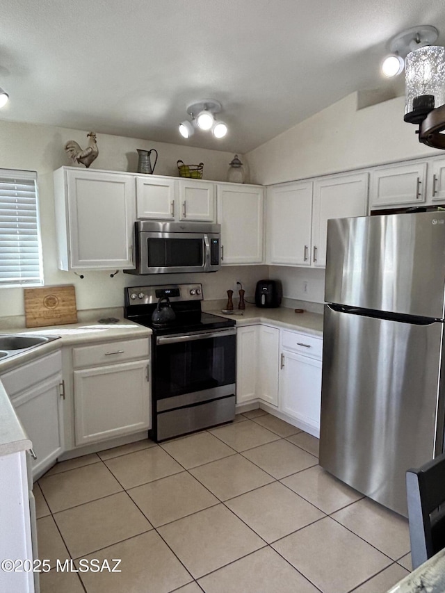 kitchen featuring vaulted ceiling, appliances with stainless steel finishes, light tile patterned flooring, white cabinetry, and sink