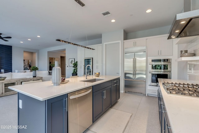 kitchen with a center island with sink, sink, range hood, appliances with stainless steel finishes, and white cabinetry