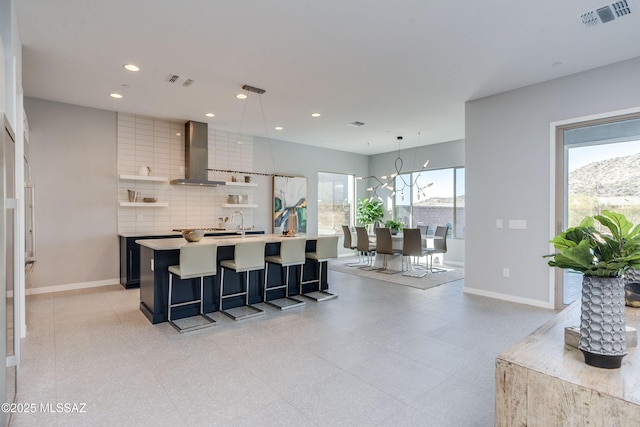 kitchen featuring pendant lighting, a center island with sink, wall chimney range hood, tasteful backsplash, and a kitchen bar