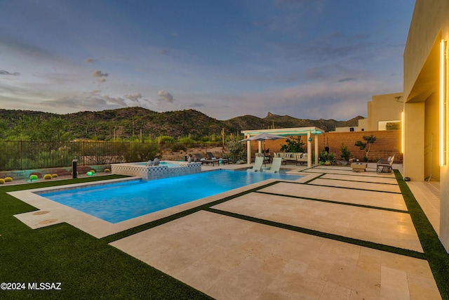 pool at dusk with a mountain view, a patio area, and an in ground hot tub