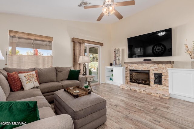 living room featuring vaulted ceiling, ceiling fan, light hardwood / wood-style floors, and a stone fireplace