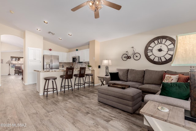 living room with ceiling fan, vaulted ceiling, and light hardwood / wood-style floors