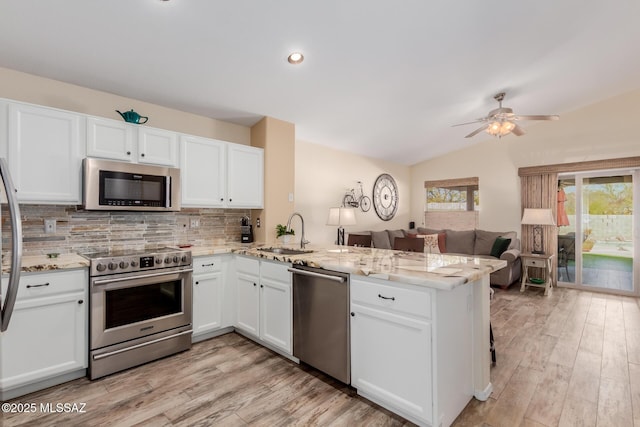 kitchen featuring kitchen peninsula, stainless steel appliances, tasteful backsplash, white cabinets, and sink