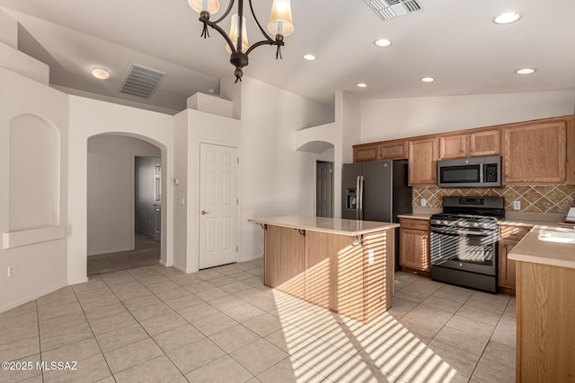 kitchen with appliances with stainless steel finishes, a center island, light tile patterned floors, pendant lighting, and decorative backsplash