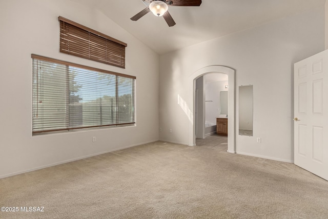 unfurnished bedroom featuring vaulted ceiling, ensuite bathroom, light colored carpet, and ceiling fan