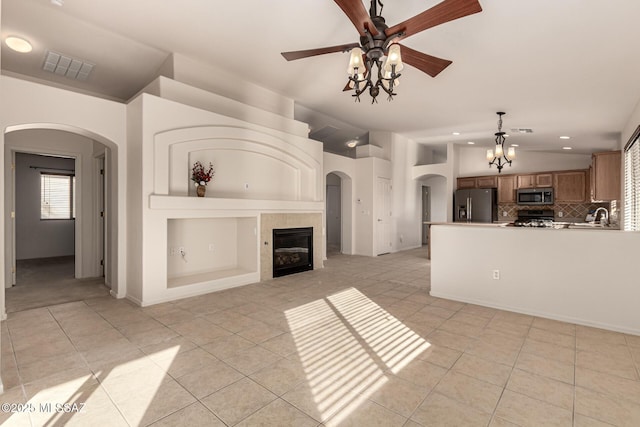 unfurnished living room with vaulted ceiling, a tiled fireplace, light tile patterned floors, sink, and ceiling fan with notable chandelier