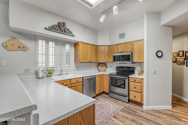 kitchen featuring sink, a high ceiling, light hardwood / wood-style flooring, stainless steel appliances, and rail lighting