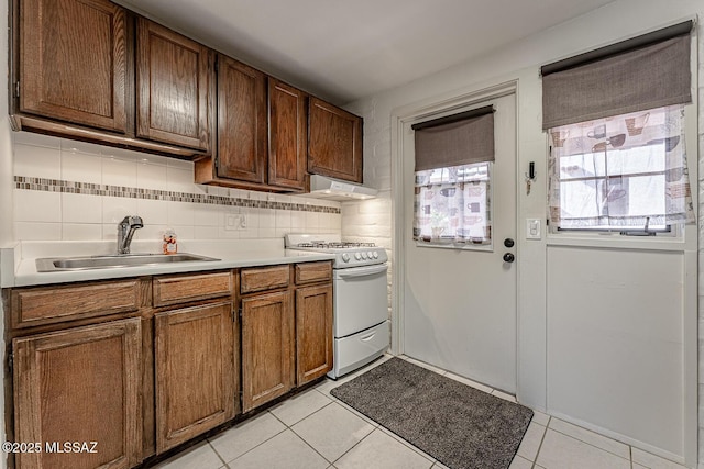 kitchen with sink, light tile patterned flooring, white gas range, and backsplash