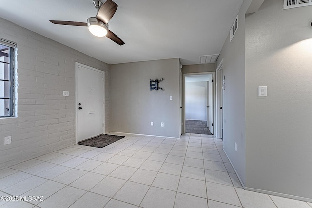 empty room featuring brick wall, light tile patterned flooring, and ceiling fan