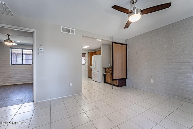 empty room featuring brick wall, ceiling fan, and light tile patterned floors