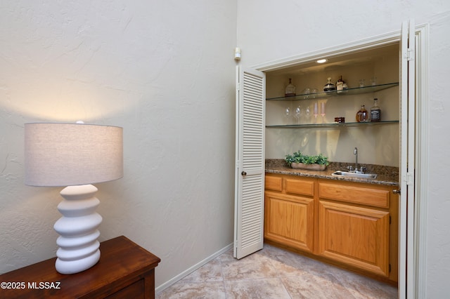 bar featuring light tile patterned floors, baseboards, a textured wall, wet bar, and a sink