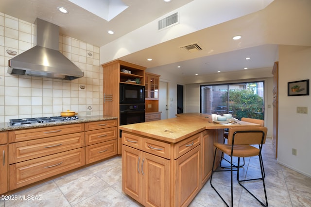 kitchen with visible vents, black appliances, wood counters, and wall chimney exhaust hood