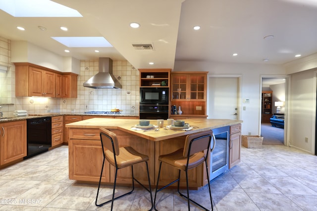 kitchen with a skylight, wooden counters, beverage cooler, wall chimney exhaust hood, and black appliances