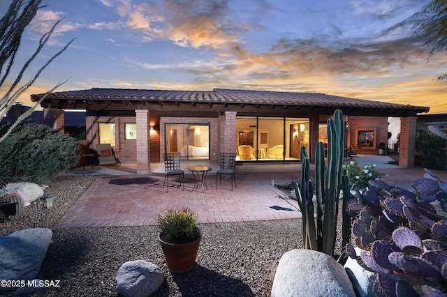 back of house at dusk featuring a patio area and brick siding