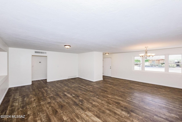 empty room featuring a textured ceiling, a notable chandelier, and dark hardwood / wood-style flooring