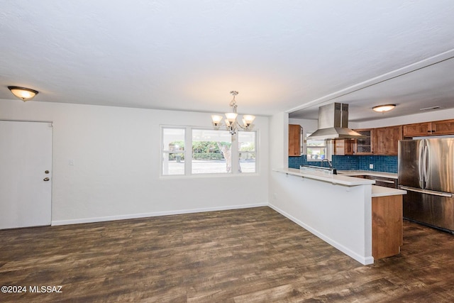 kitchen with island exhaust hood, kitchen peninsula, stainless steel refrigerator, backsplash, and pendant lighting