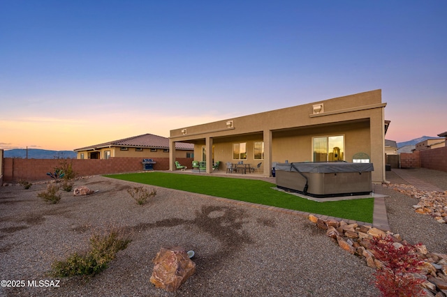 back house at dusk featuring a hot tub and a patio