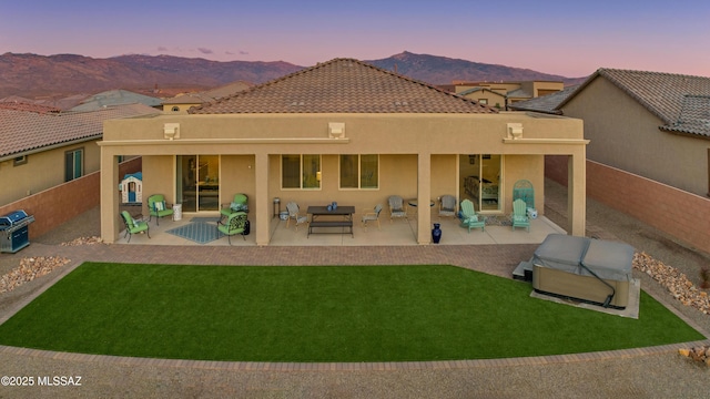 back house at dusk featuring a yard, a mountain view, and a patio area