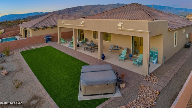 back of property with a mountain view, a patio area, and a hot tub