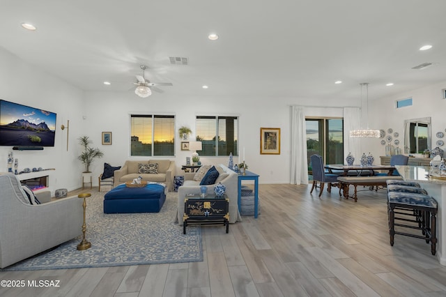 living room featuring plenty of natural light, ceiling fan with notable chandelier, and light wood-type flooring