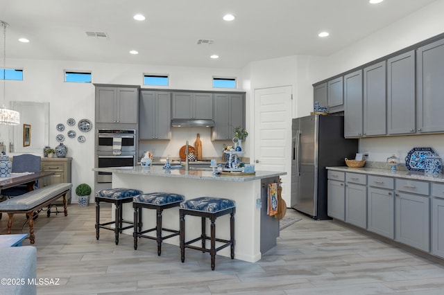 kitchen with appliances with stainless steel finishes, gray cabinets, and a center island with sink