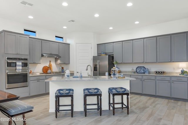 kitchen featuring gray cabinets, stainless steel appliances, a kitchen breakfast bar, and a center island with sink