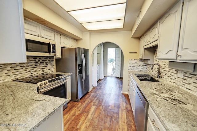 kitchen with stainless steel appliances, sink, white cabinets, decorative backsplash, and light stone countertops