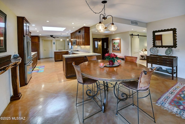 dining area featuring ceiling fan, a barn door, and a skylight