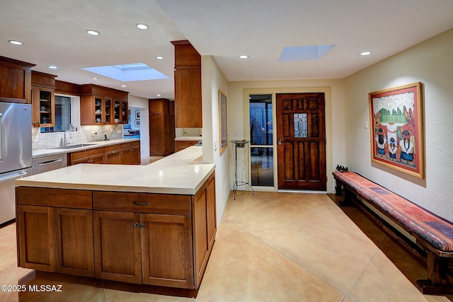 kitchen with sink, appliances with stainless steel finishes, a skylight, decorative backsplash, and kitchen peninsula