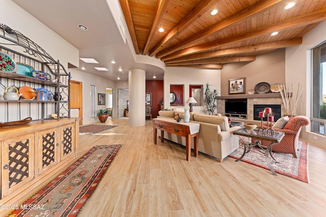 living room with beam ceiling, wooden ceiling, a tiled fireplace, light wood-type flooring, and decorative columns