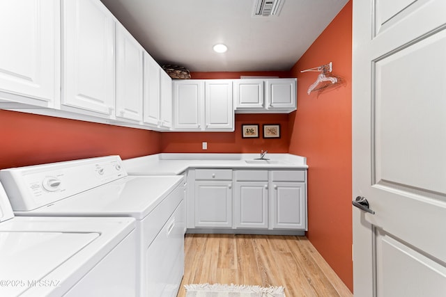 laundry room featuring sink, light wood-type flooring, independent washer and dryer, and cabinets