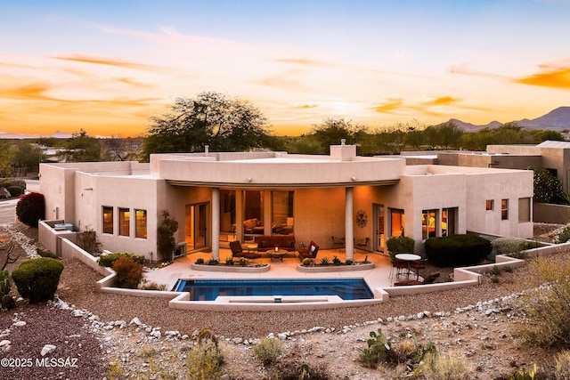 back house at dusk with an outdoor living space, a mountain view, and a patio