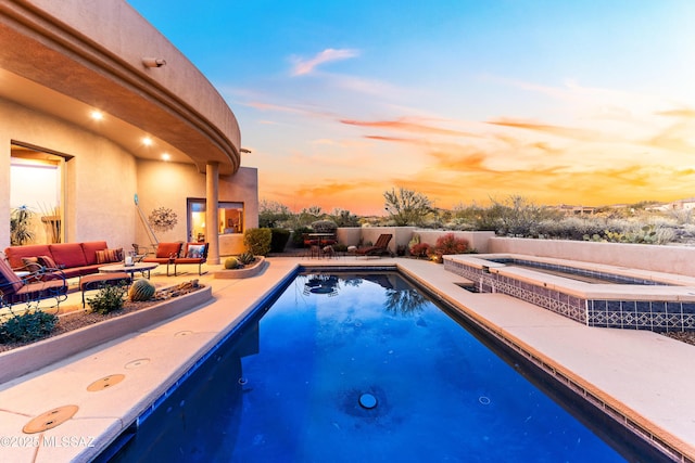 pool at dusk with an in ground hot tub, a patio area, and an outdoor hangout area