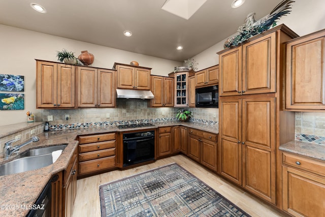 kitchen featuring black appliances, decorative backsplash, sink, light hardwood / wood-style flooring, and stone counters