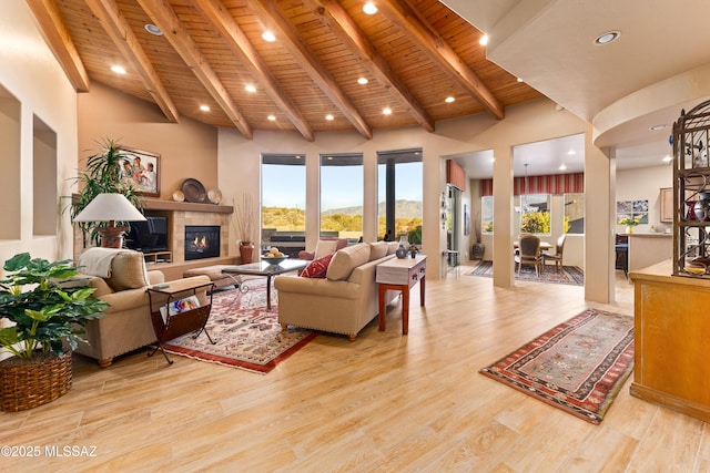 living room with a high ceiling, wood ceiling, beamed ceiling, light hardwood / wood-style floors, and a tiled fireplace