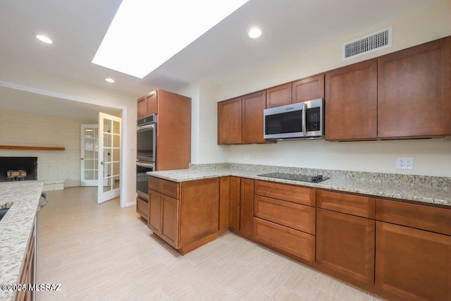 kitchen featuring a large fireplace, appliances with stainless steel finishes, a skylight, and light stone counters