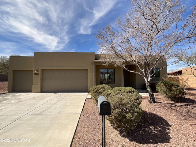 pueblo-style house with a garage, concrete driveway, and stucco siding