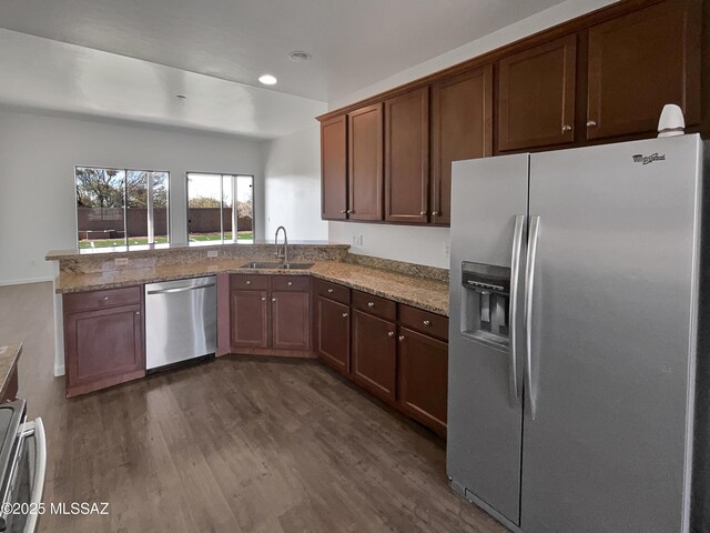 kitchen with light stone countertops, dark wood finished floors, stainless steel appliances, and a sink