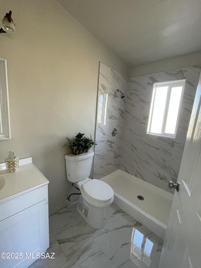 bathroom with tiled shower, vanity, and toilet