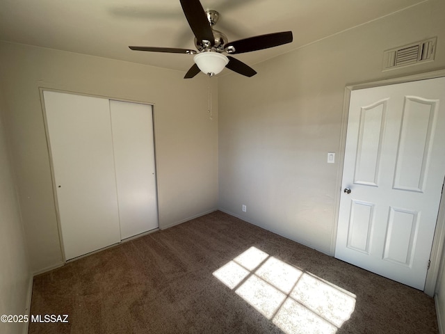 unfurnished bedroom with dark colored carpet, ceiling fan, and a closet