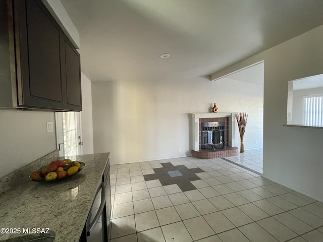 kitchen with light stone counters, a fireplace, light tile patterned flooring, and dark brown cabinets