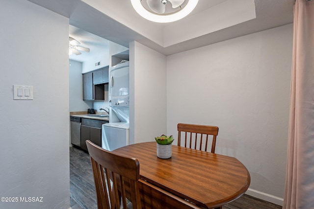 dining area with sink, stacked washer / dryer, a raised ceiling, ceiling fan, and dark wood-type flooring