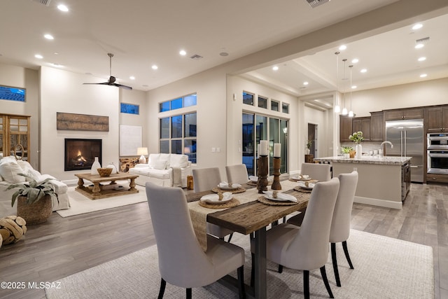 dining area featuring beamed ceiling, light hardwood / wood-style floors, ceiling fan, and a high ceiling