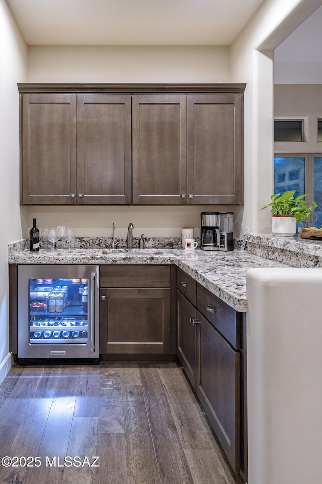 bar featuring sink, dark brown cabinets, dark hardwood / wood-style floors, wine cooler, and light stone counters