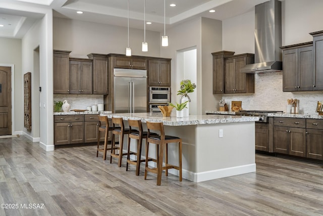 kitchen with extractor fan, a center island with sink, a towering ceiling, stainless steel appliances, and light stone countertops